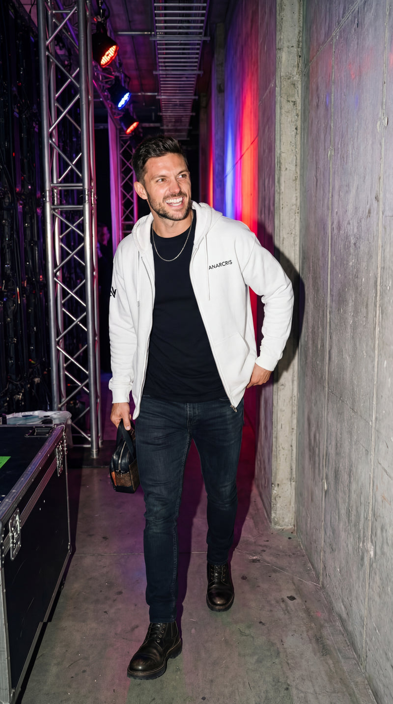 Man in a white jacket and black pants standing in a dimly lit room with colorful lighting.